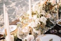 a boho beach wedding table with a macrame runner, greenery and neutral blooms, neutral candles and porcelain
