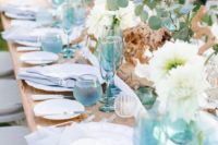 a bold and airy beach wedding tablescape with blue glasses, napkins and porcelain, white blooms, driftwood and greenery