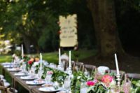 a bold and fresh summer wedding table with lots of greenery, pink blooms, white candles and blue linens