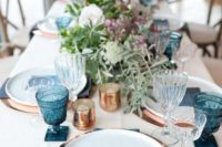 a bold beach wedding tablescape with copper placemats, white porcelain, blue glasses, menus and napkins, greenery and blooms