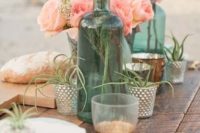 a bright beach tablescape with an uncovered table, bright peachy blooms, neutra porcelain, air pants and green bottles as vases