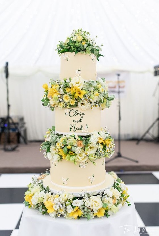 a bright summer wedding cake with floral tiers and white and yellow blooms and greenery between the tiers