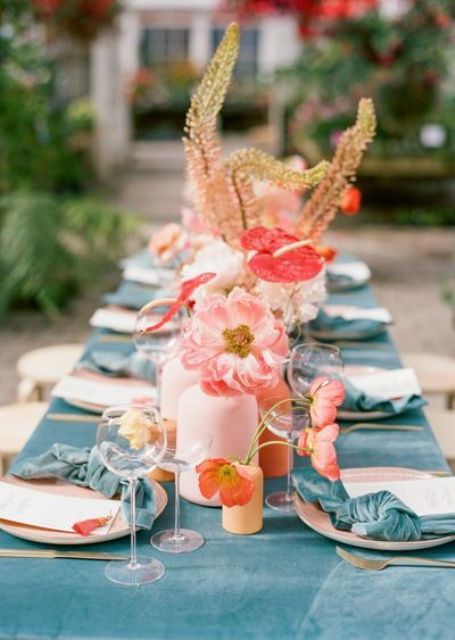 a bright summer wedding tablescape with chic blue linens, pink and red blooms and branches and gold cutlery