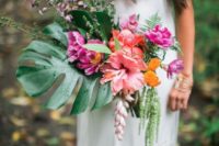 a bright tropical beach wedding bouquet of a monstera leaf, coral and hot pink blooms plus greenery