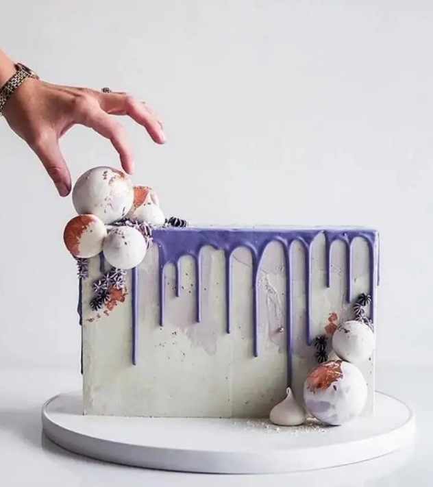 a cake top forward wedding cake with purple drip, white chocolate spheres, meringue kisses and gold pearls for a bold modern wedding