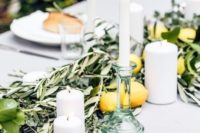 a chic Italian summer wedding tablescape with olive greenery, lemons and limes, candles and bread on the plates