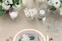 a chic neutral wedding tablescape with neutral linens, gold chargers and cutlery, neutral blooms and candles