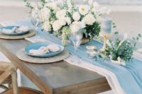 a coastal tablescape with two airy table runners, blue and neutral plates, blue candles and a neutral floral centerpiece