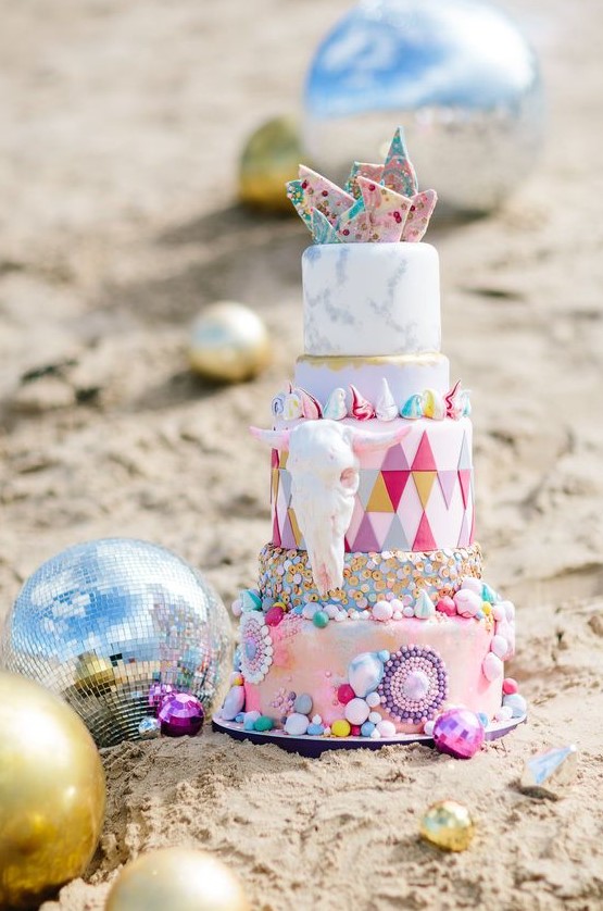 a colorful and crazy wedding cake with mismatching and bright detailed tiers, with colorful shards and a faux skull for a Burning Man wedding