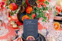 a colorful dramatic summer wedding table with a printed tablecloth, a super bold floral centerpiece with fruits, gold porcelain and cutlery