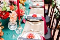 a colorful dramatic summer wedding tablescape with a turquoise runner, red candles and napkins and bright blooms