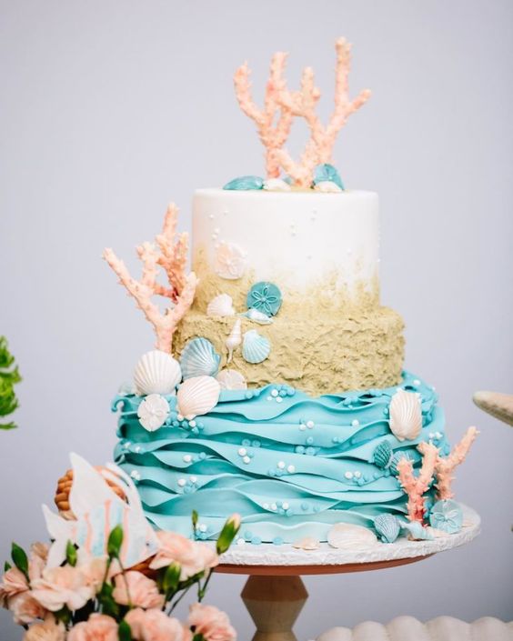 a colorful wedding cake with a white, beach sand and blue wave tier, seashells, corals, bubbles is a stunning idea for a beach wedding