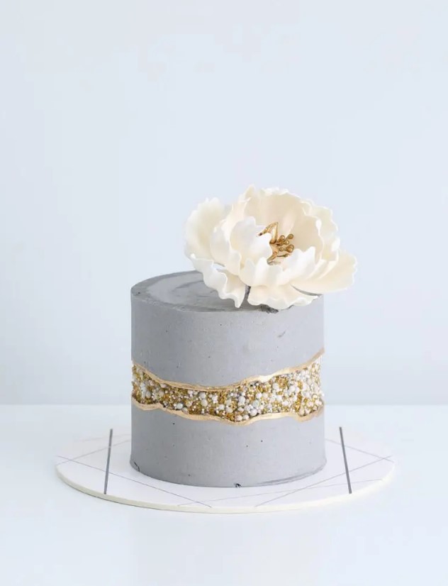 a concrete-style wedding cake with a fault line done with gold sparkles and edible beads plus a large white sugar bloom on top