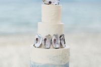 a creative ombre beach wedding cake with seashells and a black pearl is a lovely and chic idea to try