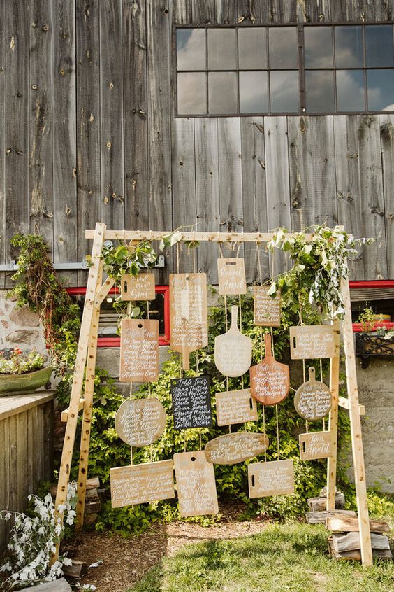 a creative rustic wedding seating chart done with cutting boards and greenery is a stylish barn idea