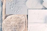 a dreamy seaside wedding invitation suite with a light grey envelope, white raw edge invites, a round tan piece and a bit of sea salt
