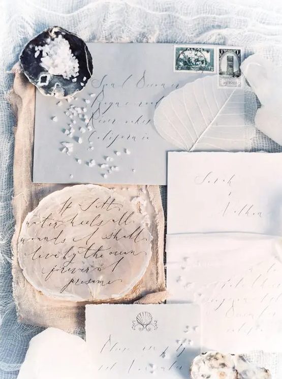 a dreamy seaside wedding invitation suite with a light grey envelope, white raw edge invites, a round tan piece and a bit of sea salt