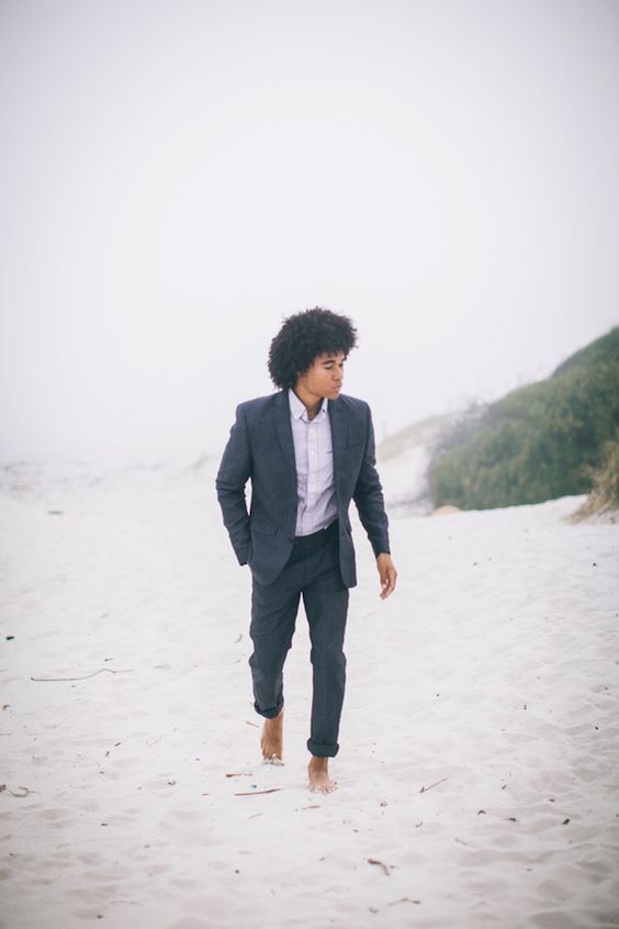 a grey suit with rolled up pants and a white shirt make up a nice outfit option for a beach wedding