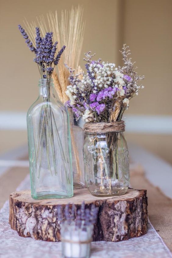 a lavender wedding centerpiece on a wood slice, with bottles and jars, baby's breath and wheat