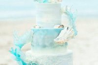a light blue beach wedding cake with sugar seashells and waves attached looks very spectacular as if it’s right out of the sea