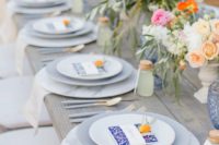 a lively summer wedding table with marble chargers, bright blooms, blue glasses and printed menus
