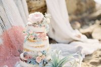 a naked beach wedding cake with blush blooms, pale greenery, seashells and an air plant is chic