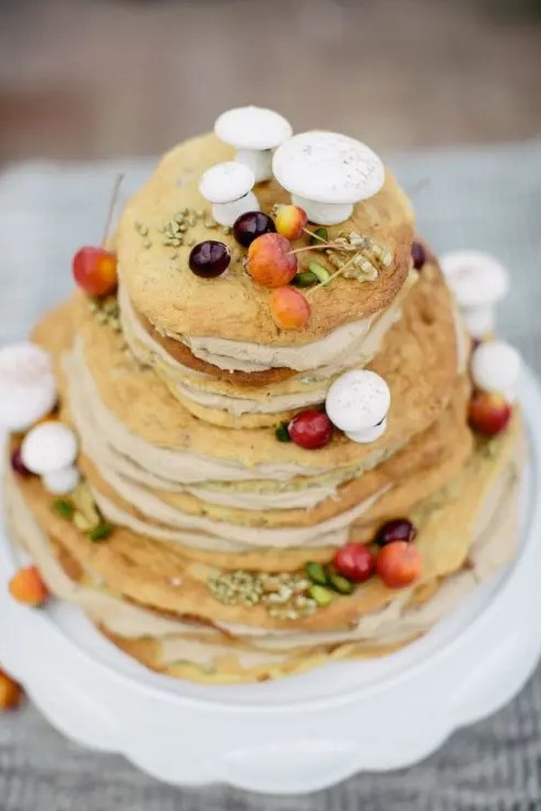 a naked wedding cake topped with blooms, berries and sugar mushrooms on top looks super natural and real