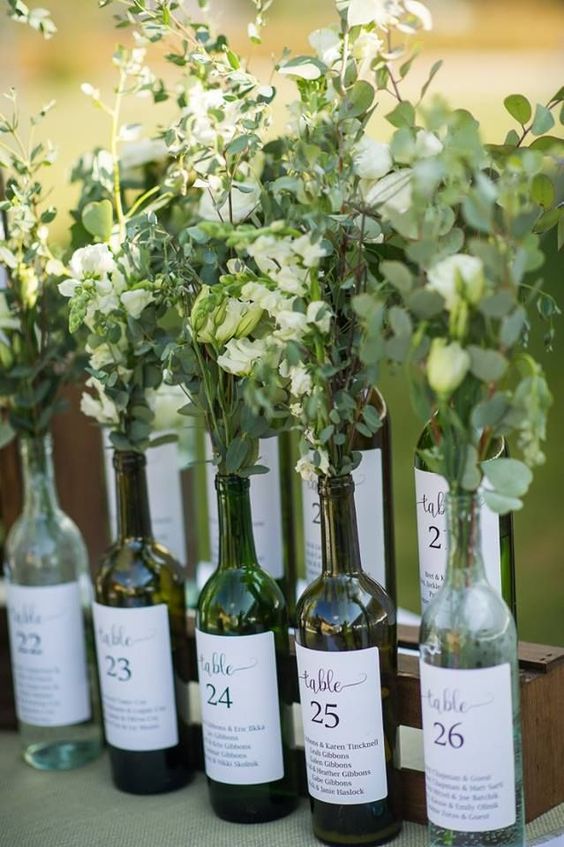 a natural wedding seatign chart with bottles and fresh greenery and white blooms plus a seating plan on them