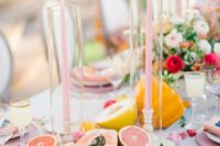 a pastel summer wedding tablescape with pink candles, lots of fruits on the table and bright blooms