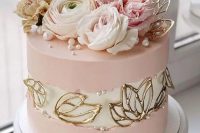 a pink wedding cake with a white fault line and gold leaves plus pearls, pink and white blooms on top