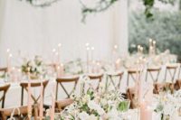 a romantic summer wedding tablescape with neutral blooms, blush candles, chic cutlery and greenery over the tables