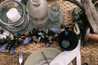 a rustic beach wedding table with grey and light green plates, driftwood, seashells, bottles and glass candleholders