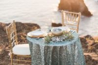 a sea glass colored sequin tablecloth, greenery, starfish and gold placemats plus gold candle lanterns and pillar candles
