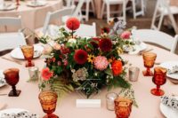 a stylish summer wedding tablescape with a bright floral centerpiece, printed napkins, colored glasses