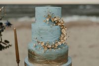 a textural blue wedding cake with gold decor – brushstrokes and gold blooms and beads is veyr refined