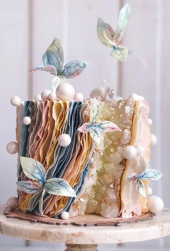 a unique wedding cake with a geode touch, layered pastel ruffles, mini snowballs, pastel sugar blooms is a lovely idea