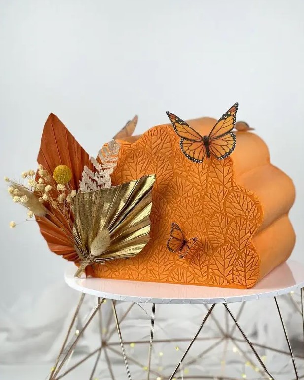 a wavy orange cake top forward wedding cake decorated with gilded fronds, billy balls, orange fur butterflies for a magical and unique wedding with a bold color scheme