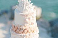 a whimsical white beach wedding cake decorated with sugar seashells, roses and corals and some thin candles on top