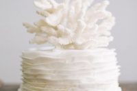 a white ruffle wedding cake with a large coral on top feels very coastal and beachy and looks very elegant