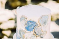 a white wedding cake decorated with blue and grey geode slices with a gold edge is a lovely and chic coastal idea