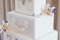 a white wedding cake featuring vintage suitcase tiers and bright fresh blooms for a bold look