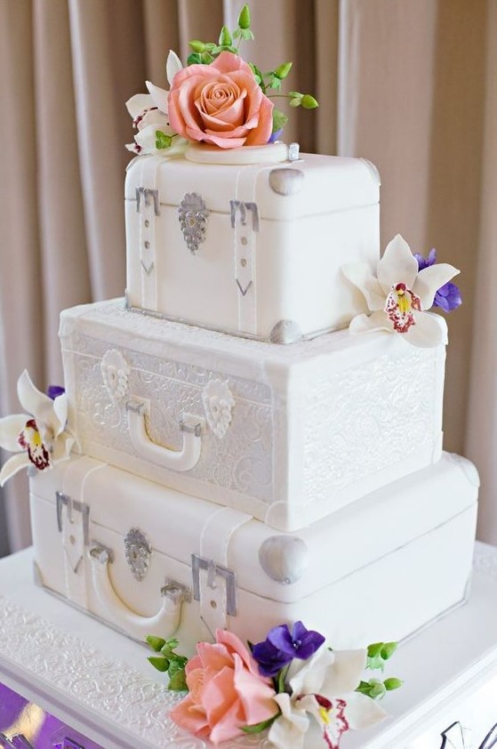 a white wedding cake featuring vintage suitcase tiers and bright fresh blooms for a bold look