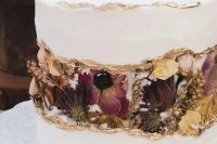 a white wedding cake with a gold edge and a fault line covered with dried blooms and foliage is very refined