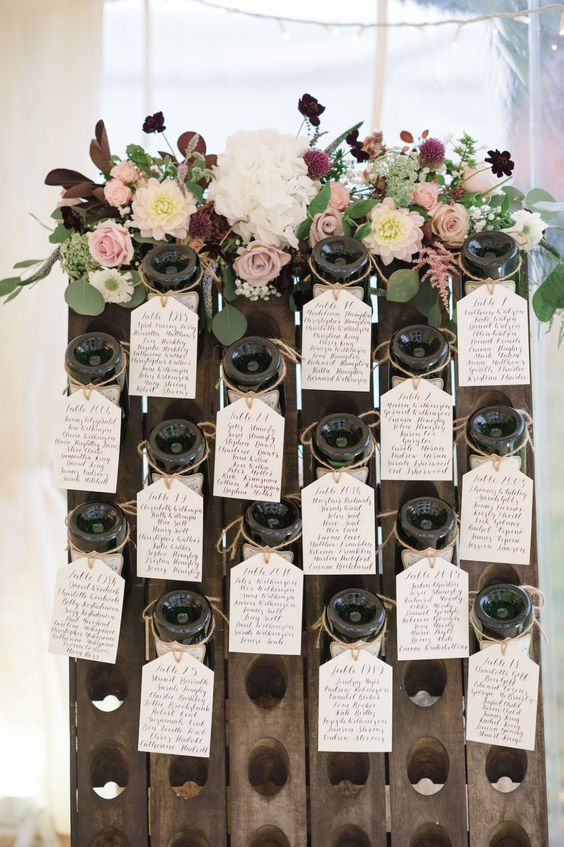 a winery wedding seating chart with bottles and bright blooms and greenery is a chic idea