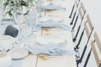an ethereal light blue wedding table with a fabric runner and matching napkins, gilded cutlery, pebbles and neutral blooms