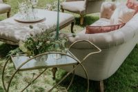 a beautiful and exquisite neutral wedding lounge with elegant seating furniture, a glass and brass bar cart, blooms and greenery and a green candle