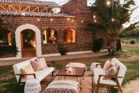 a boho outdoor wedding lounge with white sofas, a hairpin leg table, Moroccan poufs, a printed rug and some printed pillows