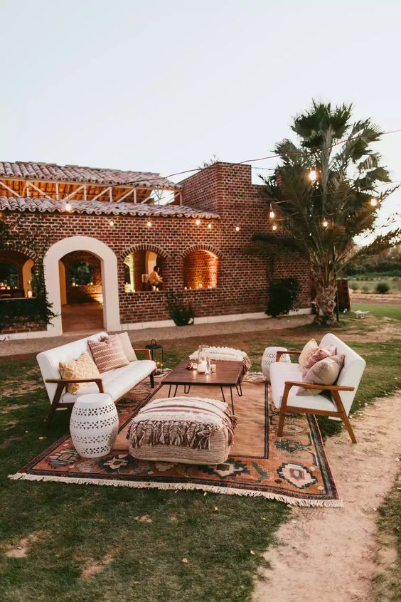 a boho outdoor wedding lounge with white sofas, a hairpin leg table, Moroccan poufs, a printed rug and some printed pillows