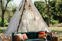 a boho wedding lounge with a green sofa, rattan chairs, a bench and a round coffee table, bright pillows and a doily teepee over the sofa