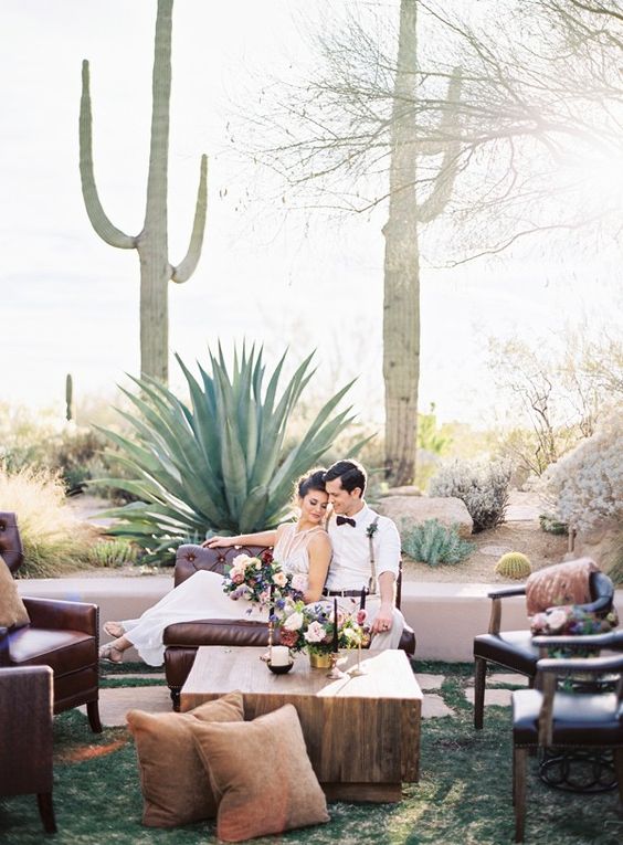 a boho wedding lounge with leather seating furniture, a low coffee table, earthy-tone pillows and bold blooms and candles